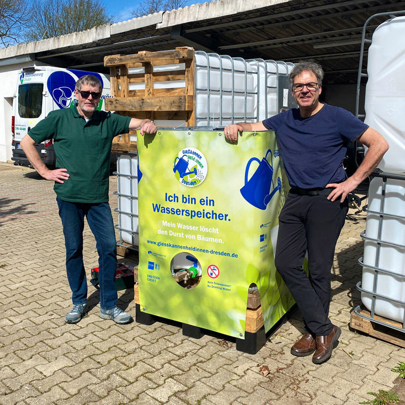 Zwei Männer proben die Aufstellung eines Wassertanks.